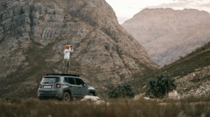 Person scans mountains from car roof.